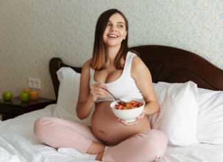 terhes nő ágyon ülve müzlit eszik