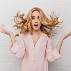 ecstatic-blue-eyed-woman-with-long-blonde-hair-posing-front-white-bricked-wall-indoor-shot-surprised-girl-beautiful-pink-pyjamas_197531-21678