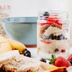 side view of overnight oats with fresh strawberries blueberries and nuts in a glass jar on rustic background