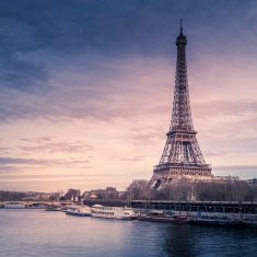 Beautiful wide shot of Eiffel Tower in Paris surrounded by water with ships under the colorful sky