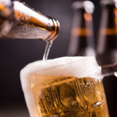 Glass bottles of beer with glass and ice on dark background
