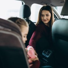 Mother with little daughter sitting in the back of the car in a car seat