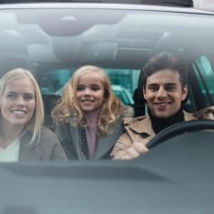 Cheerful man sitting in car with his wife and daughter
