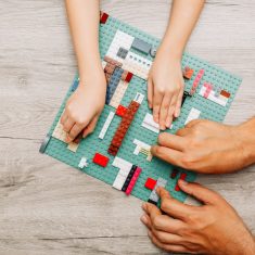 Father and daughter playing with legos on light wooden background, top view.