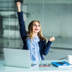 Successful young business woman with arms up at the office