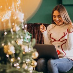 Woman sitting by Christmas tree and shopping online sales