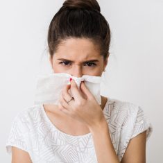 close-up portrait of pretty woman blowing her nose with napkin, catch a cold, feeling sick, isolated, white studio background, frowning