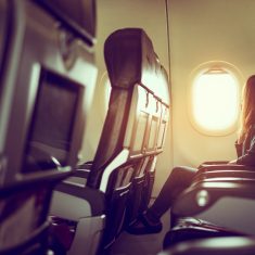 Lady is sitting in airplane looking out at bright sky through wi