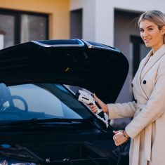 Woman charging electro car by her house and holding charger